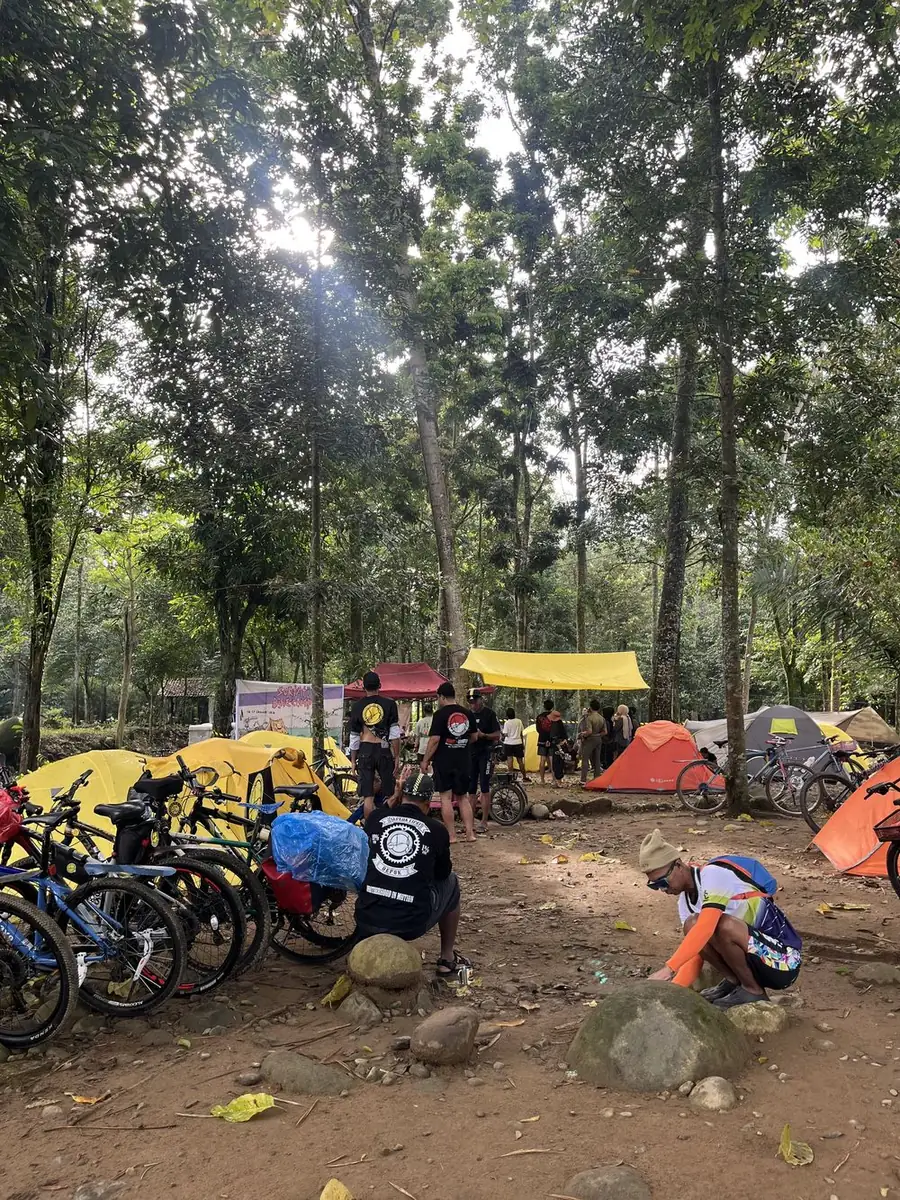 Komunitas pesepeda beristirahat di antara tenda di bawah pepohonan